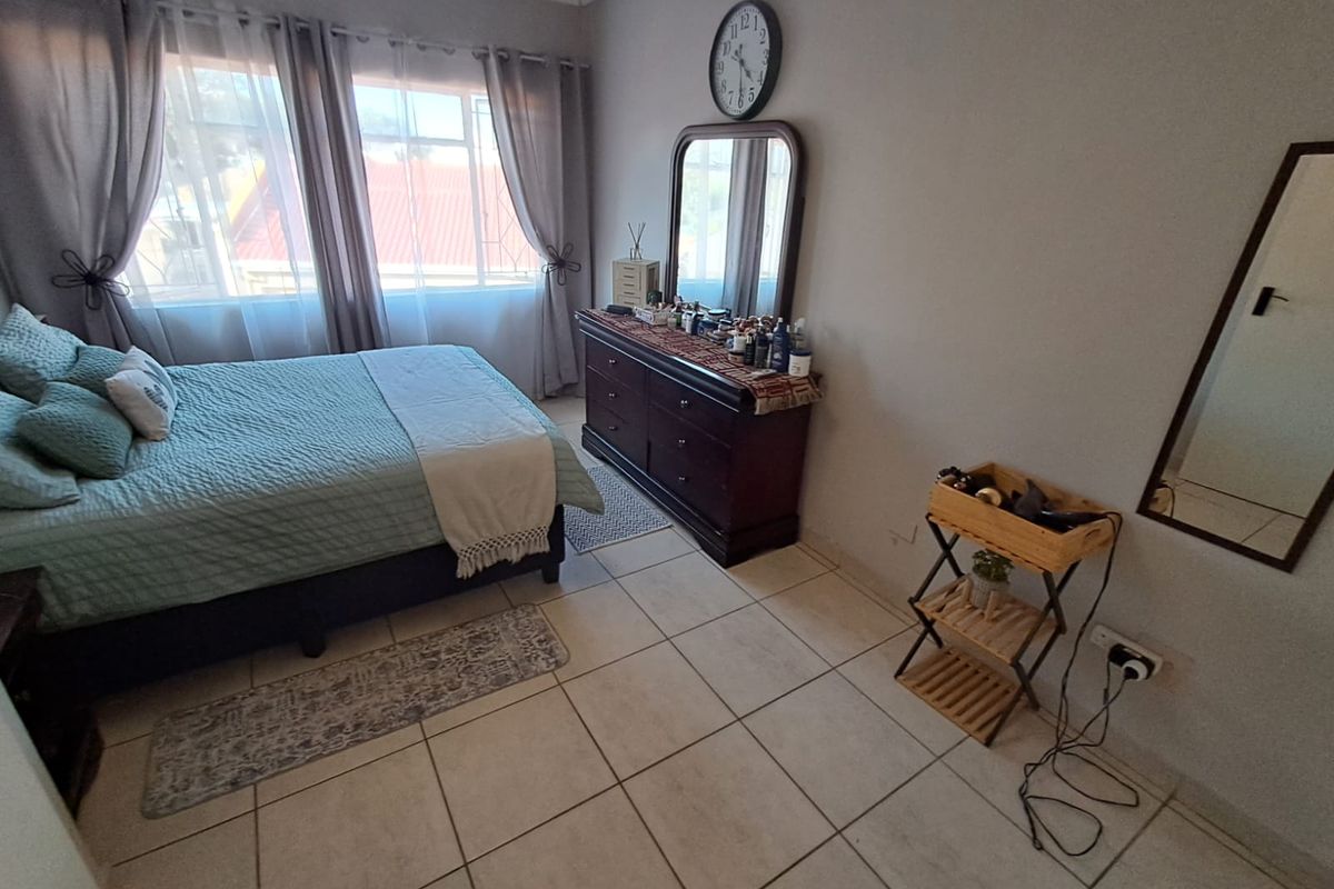 A well-lit bedroom featuring neutral tiled flooring, decorative cornice detailing, and a large window allowing for ample natural light.
