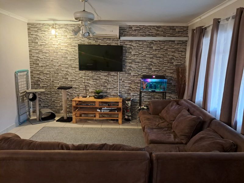 A living room featuring a textured feature wall, split-system air conditioning, ceiling fan, and tiled flooring, providing a functional and comfortable living space.
