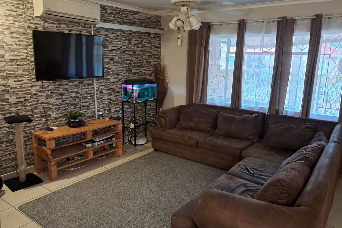 Spacious living room featuring tiled flooring, a ceiling fan, and a split-system air conditioner, with a feature wall and large windows with security gates.