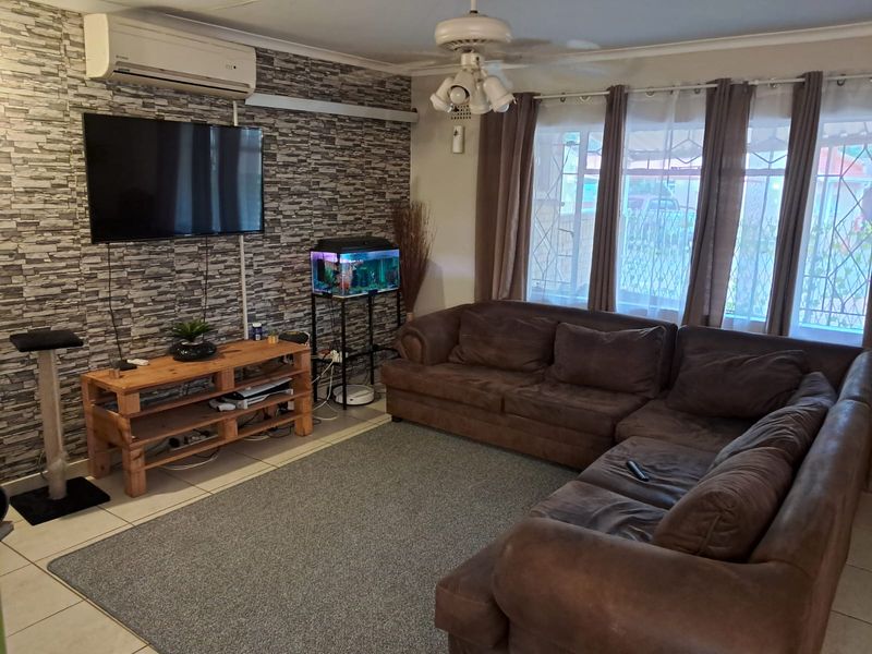 Spacious living room featuring tiled flooring, a ceiling fan, and a split-system air conditioner, with a feature wall and large windows with security gates.