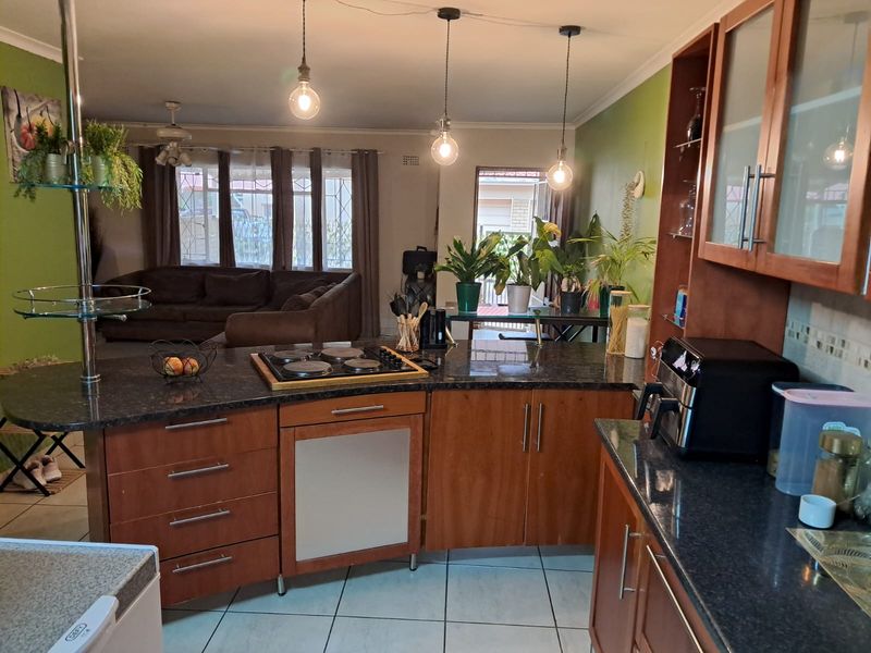 Open-plan kitchen and living area featuring granite countertops, wooden cabinetry, electric hob, and tiled flooring with direct access to an outdoor patio.