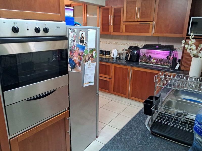 A functional kitchen featuring warm-toned laminate cabinetry, granite countertops, a built-in oven, and a double bowl sink with a mosaic tile backsplash.