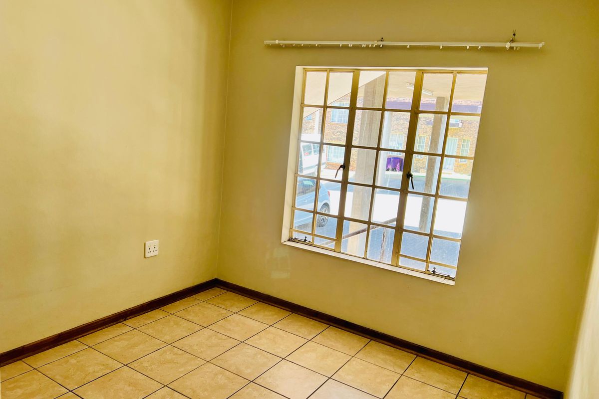 An empty bedroom featuring neutral wall paint, tiled flooring, and a window fitted with security burglar bars and a curtain rail.
