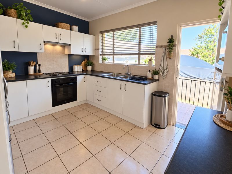 A well-maintained kitchen featuring white cabinetry, dark countertops, built-in oven and hob, tiled flooring, and direct access to an outdoor patio area.