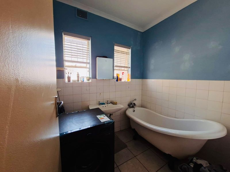 A functional bathroom featuring a classic freestanding bathtub, wall-mounted basin, and tiled splashback, requiring cosmetic updates to the wall finishes.