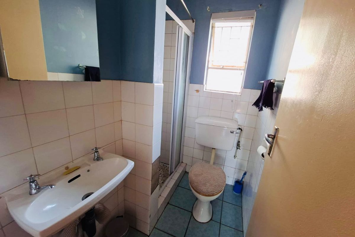 A compact bathroom featuring a pedestal basin, toilet, and shower enclosure with tiled walls and flooring, requiring cosmetic updates.