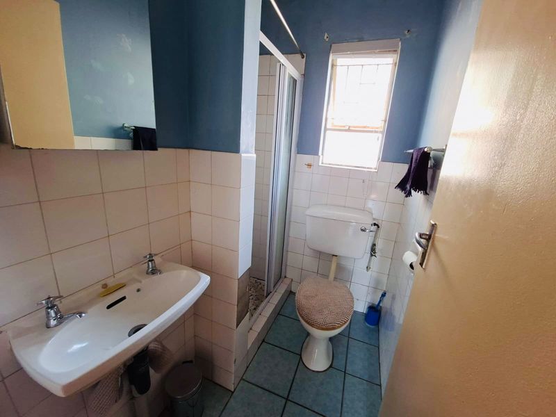 A compact bathroom featuring a pedestal basin, toilet, and shower enclosure with tiled walls and flooring, requiring cosmetic updates.