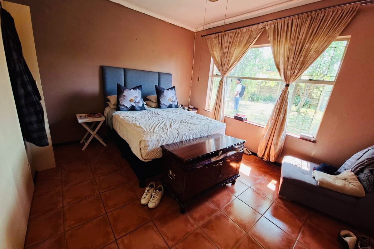 A bedroom featuring tiled flooring, a large window providing natural light, and a ceiling fan. The space offers a functional layout for rest.