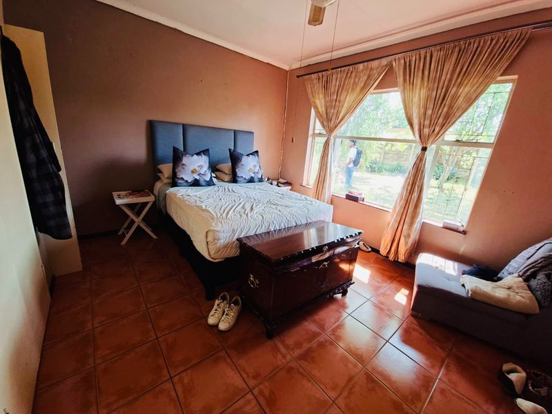A bedroom featuring tiled flooring, a large window providing natural light, and a ceiling fan. The space offers a functional layout for rest.