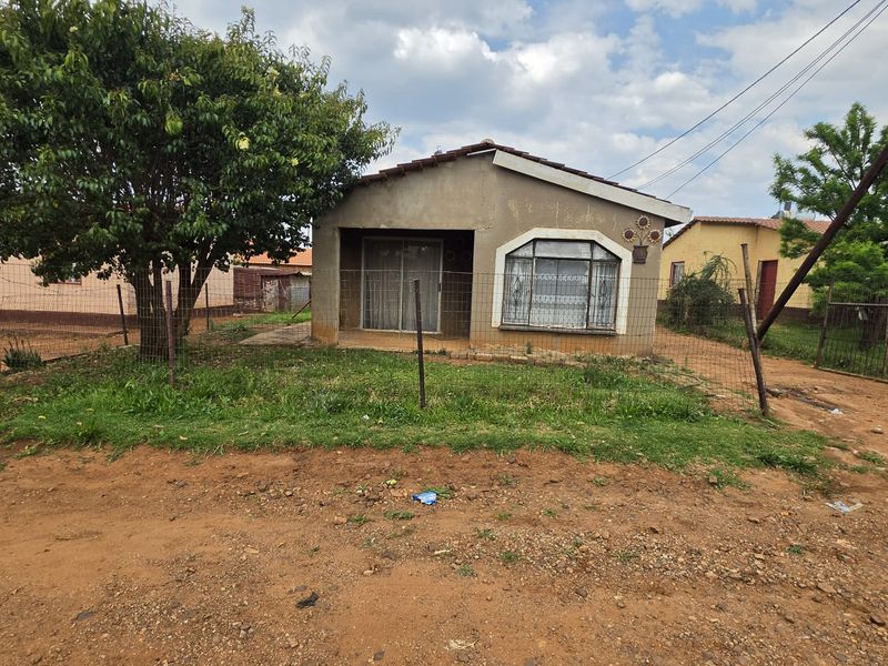 Front view of a single-story house featuring a tiled roof, security bars on windows, and a wire-fenced yard with an unpaved approach.