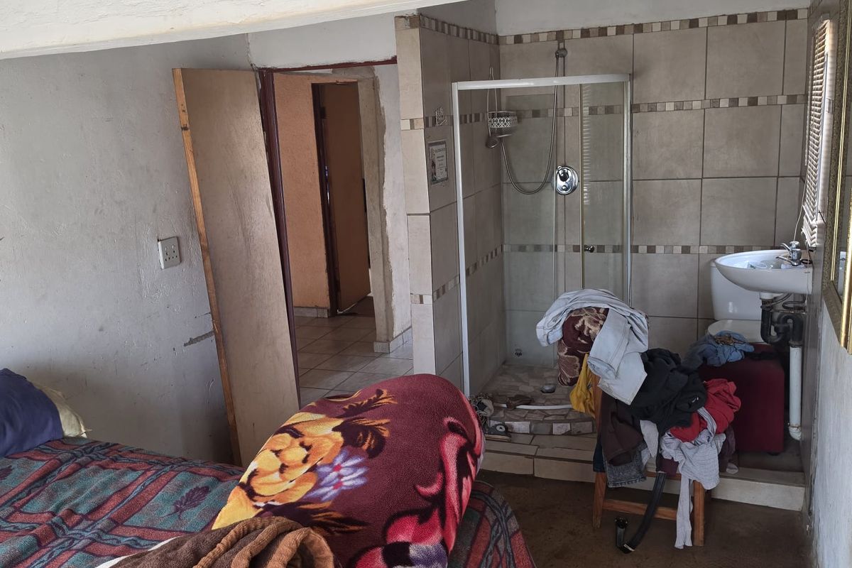 Bedroom featuring an integrated open-plan shower and basin area with tiled finishes, requiring significant maintenance and cosmetic updates to improve the overall condition.
