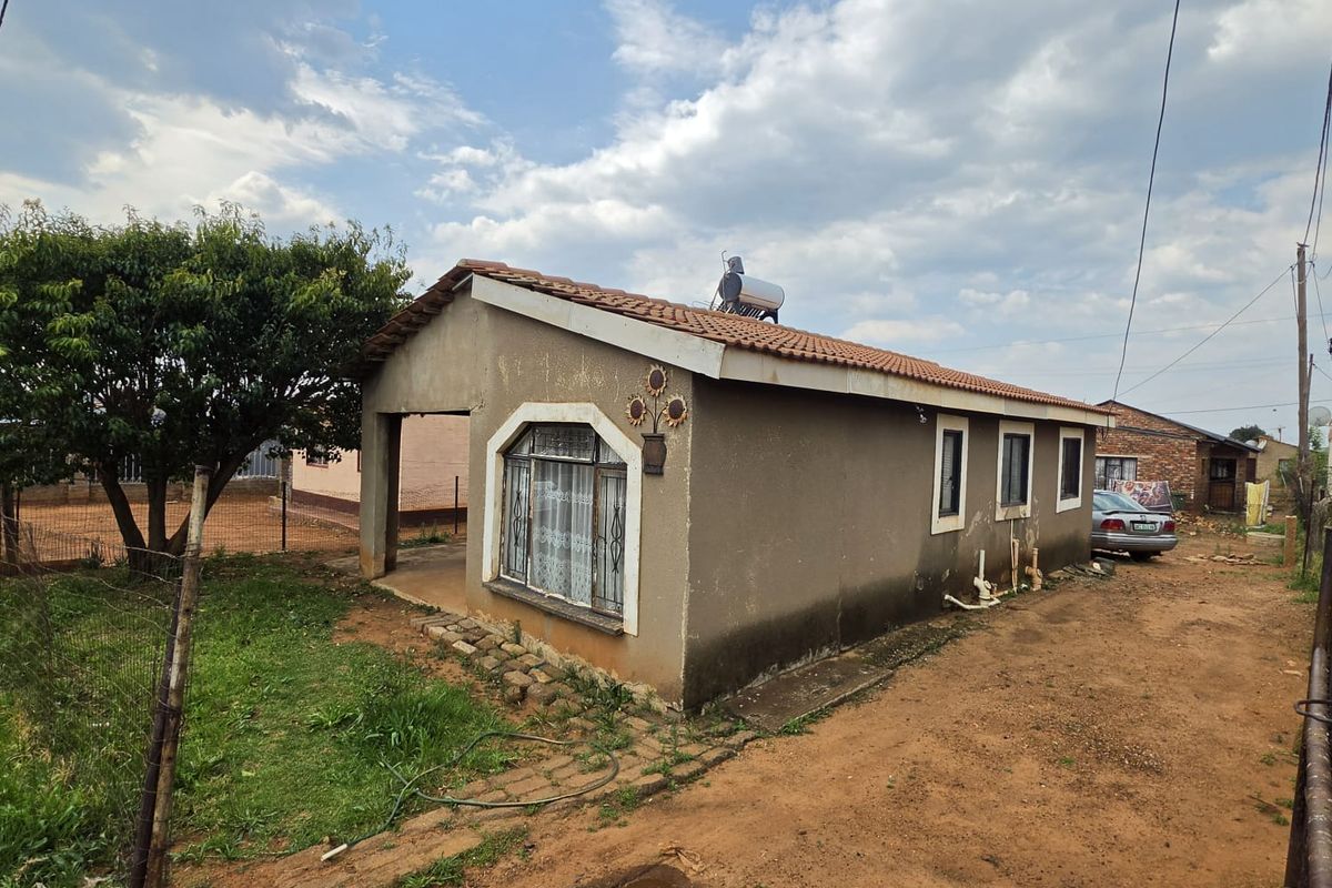 Rear view of a single-story house featuring a tiled roof, solar water heater, and a covered patio area with visible exterior wall maintenance required.