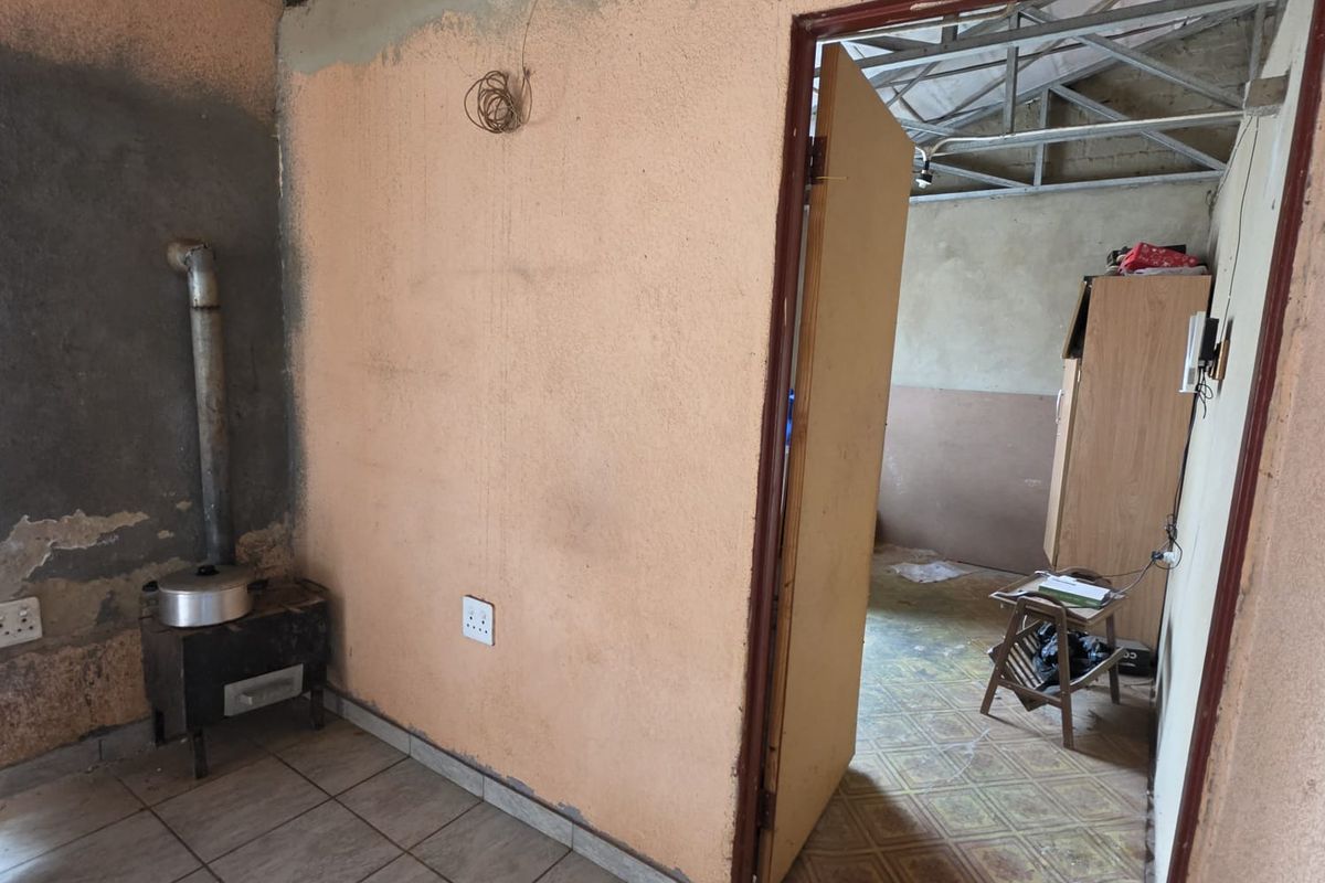 An unfinished living area featuring exposed roof trusses, tiled flooring, and a wood-burning stove, requiring significant renovation and finishing work.