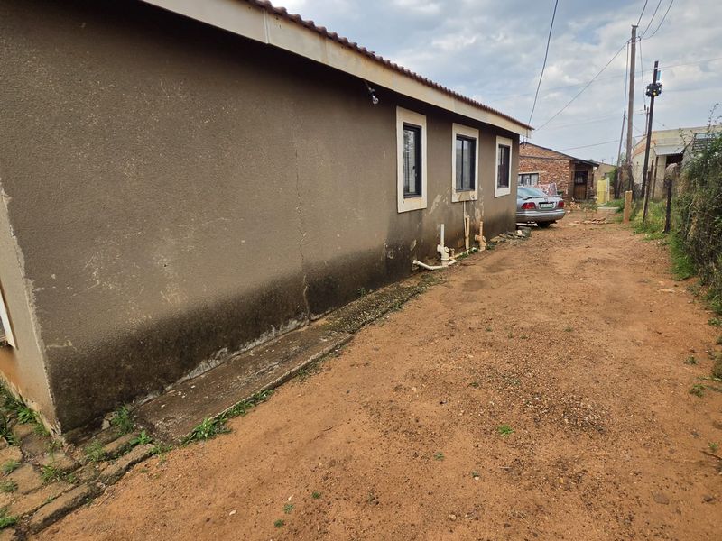Rear exterior view of the property showing plastered walls, tiled roof, and casement windows, with visible signs of wear and unpaved ground.
