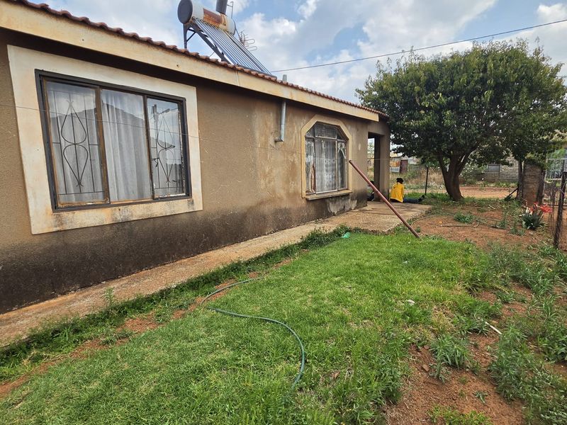 Rear exterior view of the house featuring a solar water heater, security bars on windows, and a garden area with a concrete pathway.
