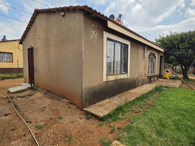 Rear view of a detached house featuring plastered walls, tiled roofing, and metal window frames, set on a plot with a small lawn area.