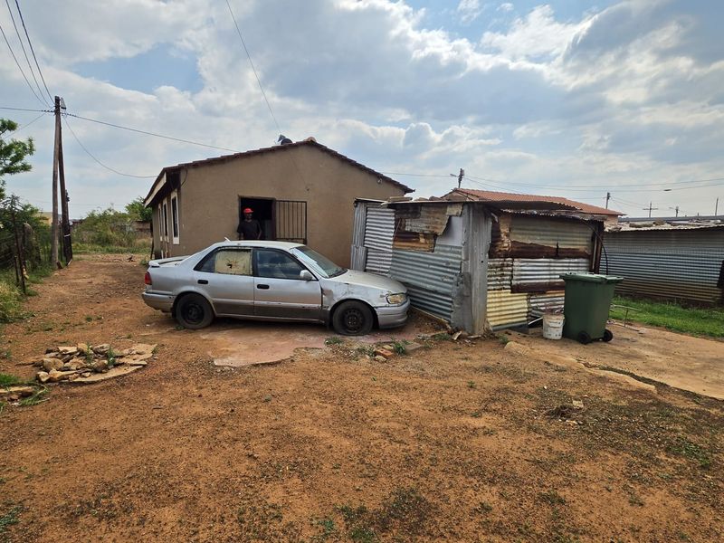 Rear exterior view of the property featuring a corrugated metal outbuilding and an unpaved yard area.