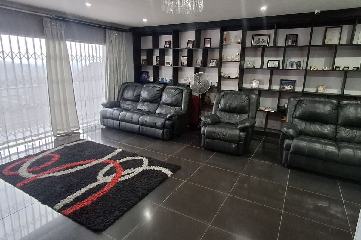 Spacious living room featuring dark tiled flooring, a large built-in display shelving unit, recessed lighting, and a decorative crystal chandelier.