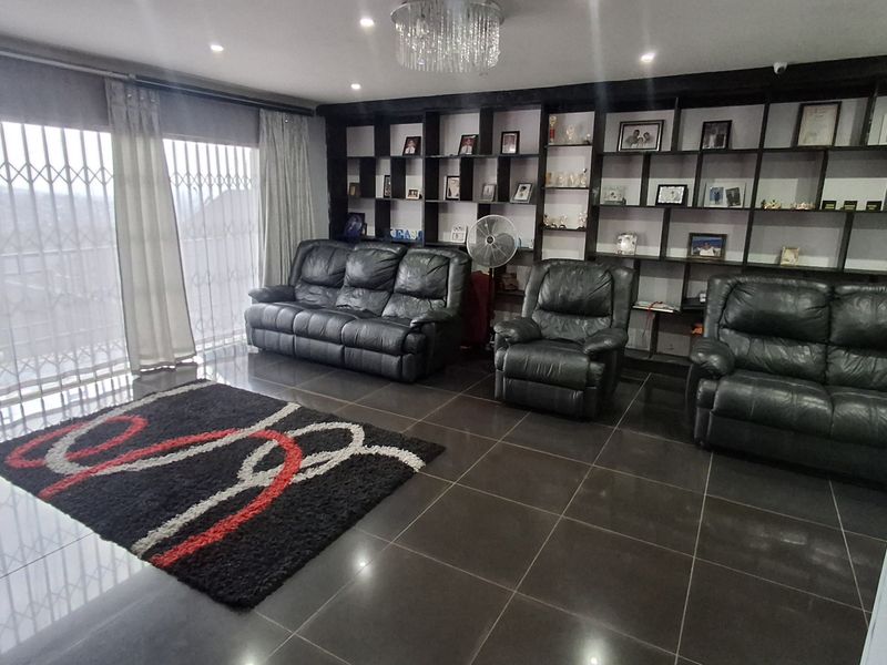 Spacious living room featuring dark tiled flooring, a large built-in display shelving unit, recessed lighting, and a decorative crystal chandelier.