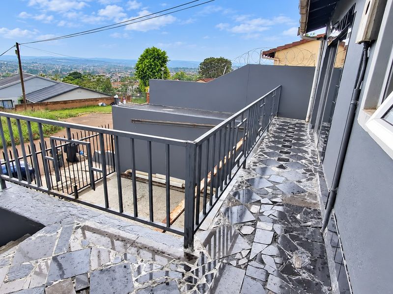 An elevated balcony area featuring metal railings and stone paving, offering expansive views of the surrounding neighborhood and landscape.