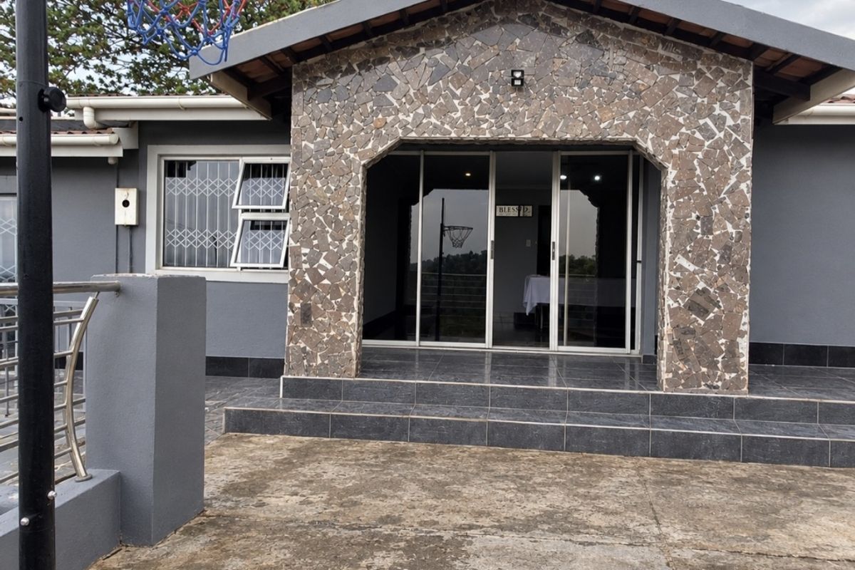 Rear exterior view featuring a stone-clad facade, sliding glass doors, and a tiled entrance leading to a concrete patio area.