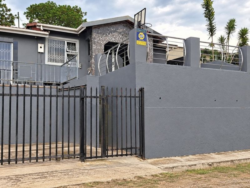 Front elevation of a residential property featuring a raised patio, stone cladding accents, and secure metal perimeter fencing.