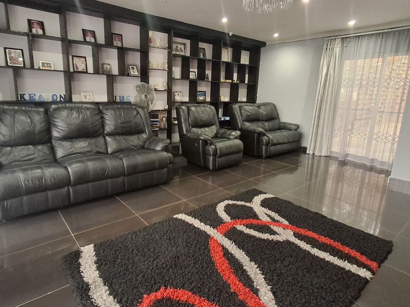 Spacious living room featuring dark tiled flooring, a large built-in display shelving unit, recessed lighting, and a decorative crystal chandelier.