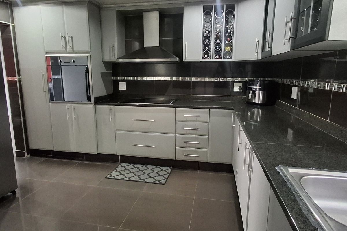 Modern kitchen featuring sleek grey cabinetry, granite countertops, built-in oven, extractor fan, and tiled flooring with a functional layout.