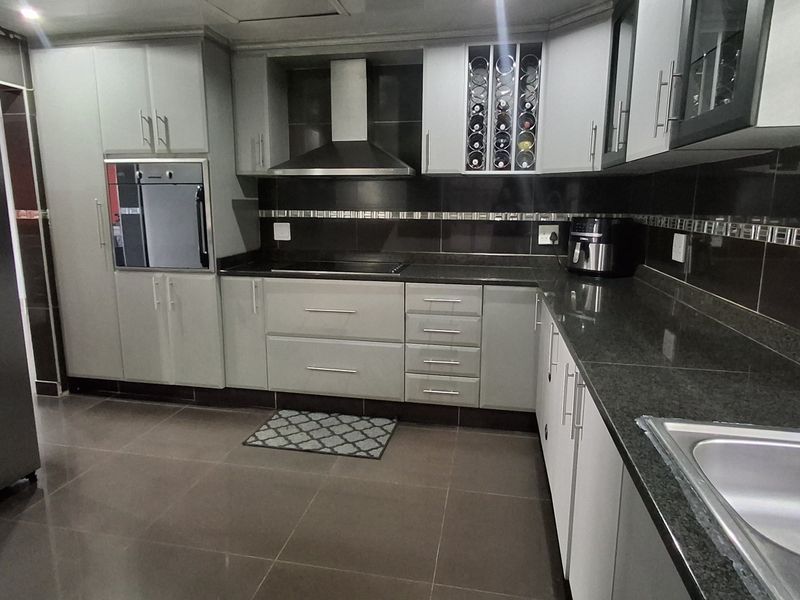 Modern kitchen featuring sleek grey cabinetry, granite countertops, built-in oven, extractor fan, and tiled flooring with a functional layout.