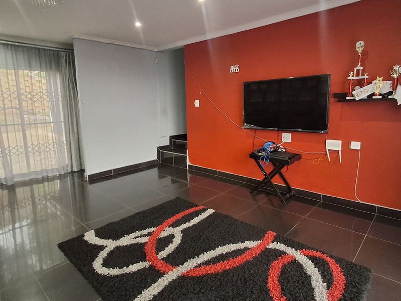 Living room featuring dark tiled flooring, recessed lighting, a decorative chandelier, and a prominent red accent wall with integrated television mounting.