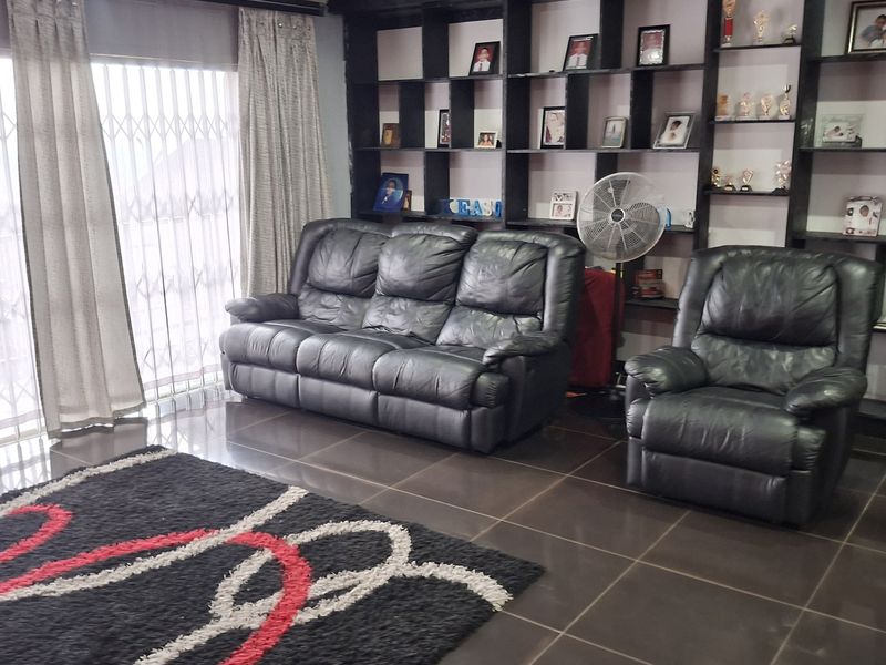 A comfortable living room featuring dark tiled flooring, recessed lighting, and a large floor-to-ceiling built-in shelving unit.