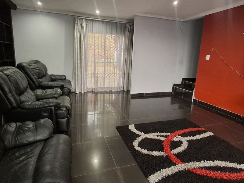Spacious living room featuring dark tiled flooring, recessed lighting, and a sliding door leading to the exterior, with a prominent red accent wall.