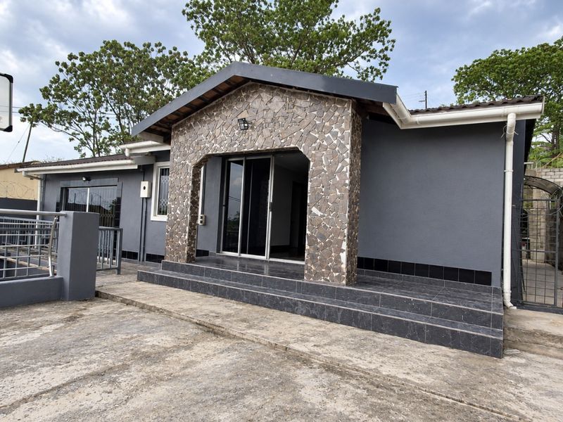 Front elevation of a modern house featuring stone cladding, dark tiled entrance steps, and sliding glass doors, set on a concrete driveway.