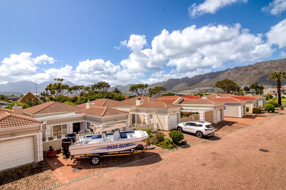 An aerial view of a residential estate featuring multiple homes with tiled roofs, paved driveways, and mountain views in the background.