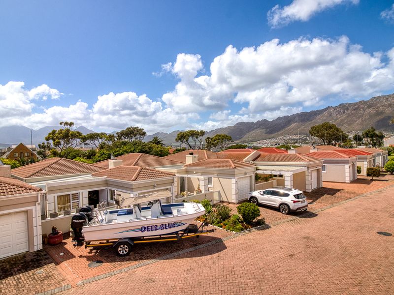 An aerial view of a residential estate featuring multiple homes with tiled roofs, paved driveways, and mountain views in the background.
