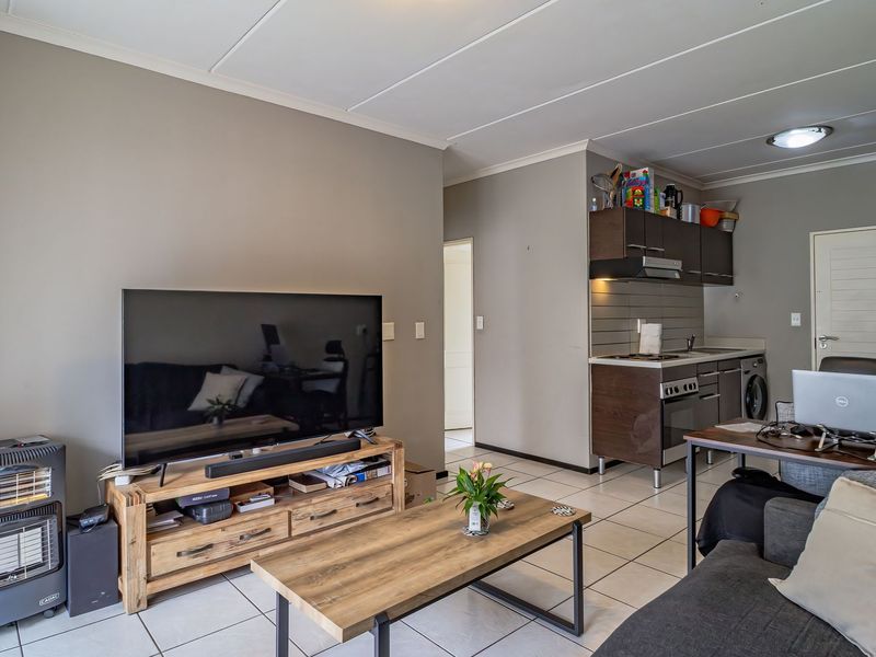 Open-plan living area featuring tiled floors and a compact kitchen with built-in cabinetry, oven, and hob.