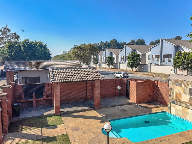 Outdoor entertainment area featuring a swimming pool, brick built-in braai, and paved patio space within a secure complex setting.