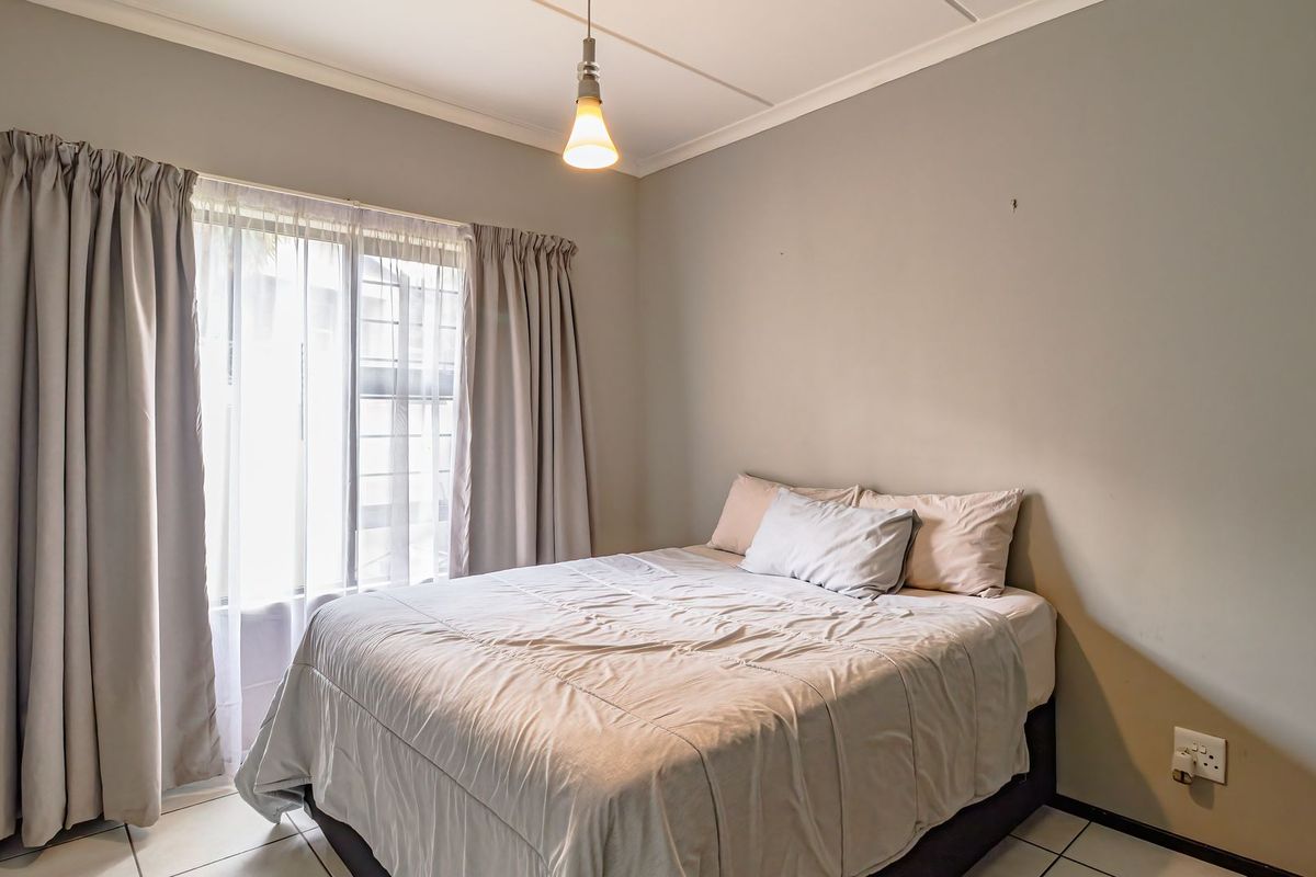A functional bedroom featuring tiled flooring, a window with security bars, and neutral wall finishes, providing a comfortable and well-lit sleeping space.
