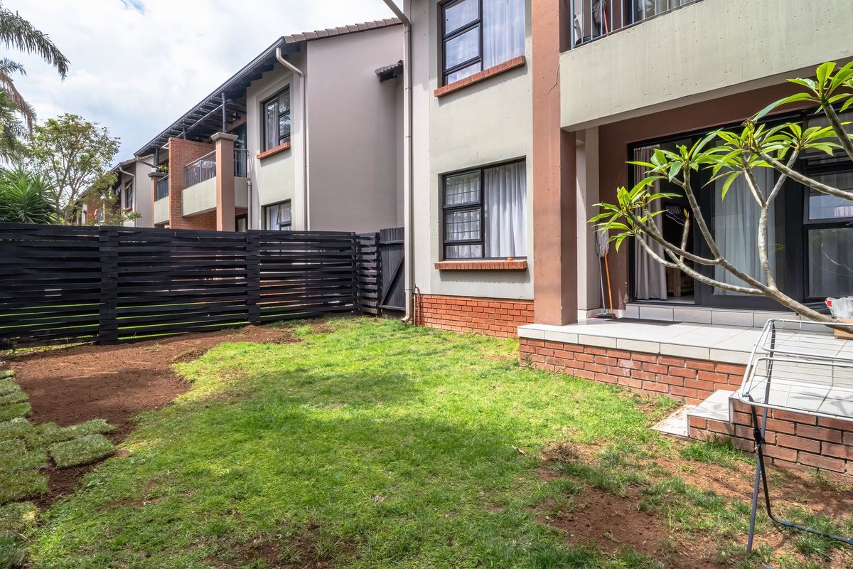 A private rear garden area featuring a tiled patio, brick foundation, and a black timber fence, providing direct access to the apartment interior.