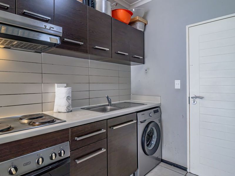 Compact kitchen featuring dark wood cabinetry, stainless steel appliances, tiled backsplash, and an integrated washing machine, providing a functional and efficient workspace.
