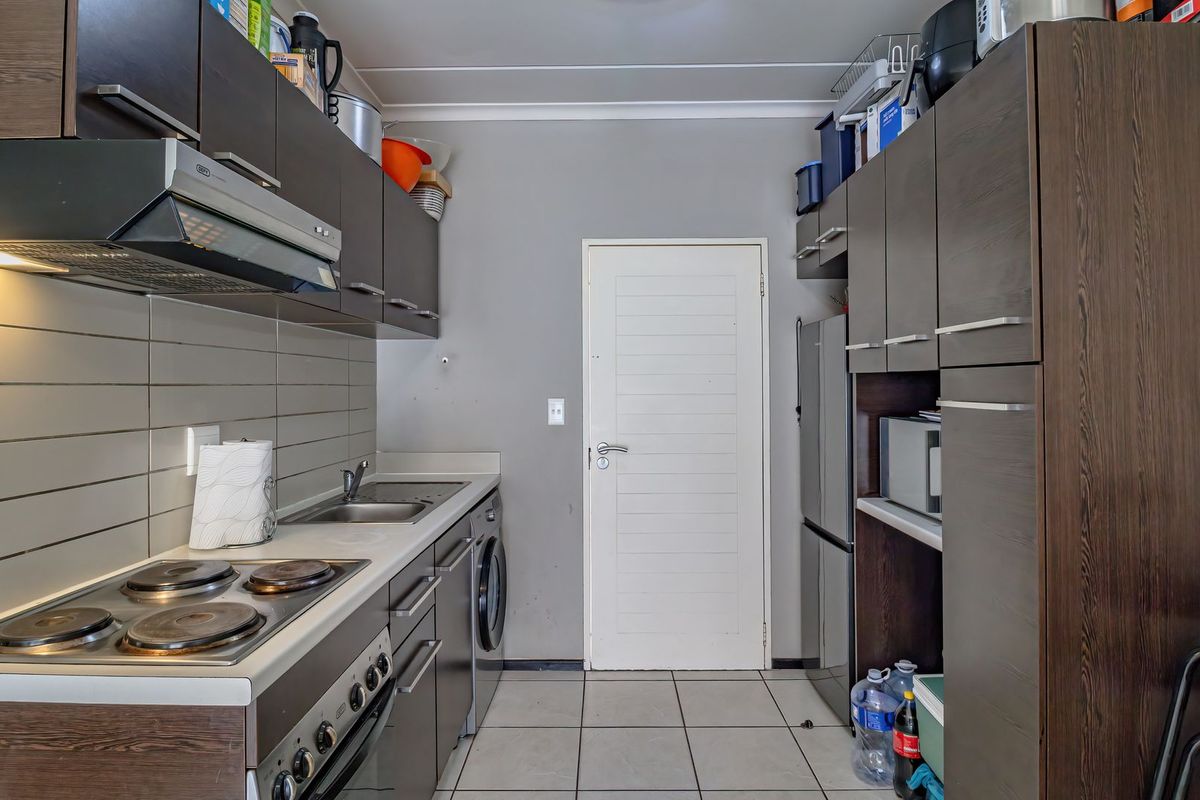 Compact kitchen featuring dark wood cabinetry, built-in oven and hob, stainless steel sink, and tiled flooring with a functional layout.