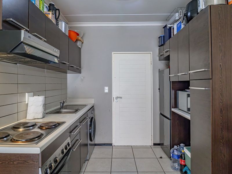 Compact kitchen featuring dark wood cabinetry, built-in oven and hob, stainless steel sink, and tiled flooring with a functional layout.