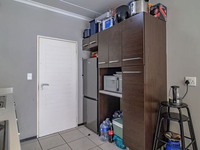 A functional kitchen featuring dark wood cabinetry, stainless steel sink, electric hob with extractor fan, and neutral tiled flooring.