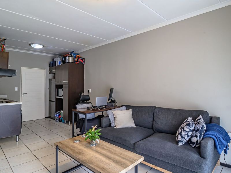 Open-plan living area featuring tiled flooring and a compact kitchen corner with built-in cabinetry and integrated cooking appliances.