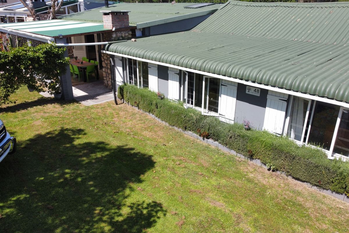Aerial view of the rear elevation featuring a corrugated metal roof, brick chimney, covered patio area, and established garden surroundings.
