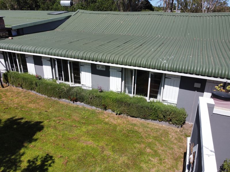 Aerial view of the rear elevation featuring a corrugated metal roof, solar water heater, and white shutters on a grey exterior wall.