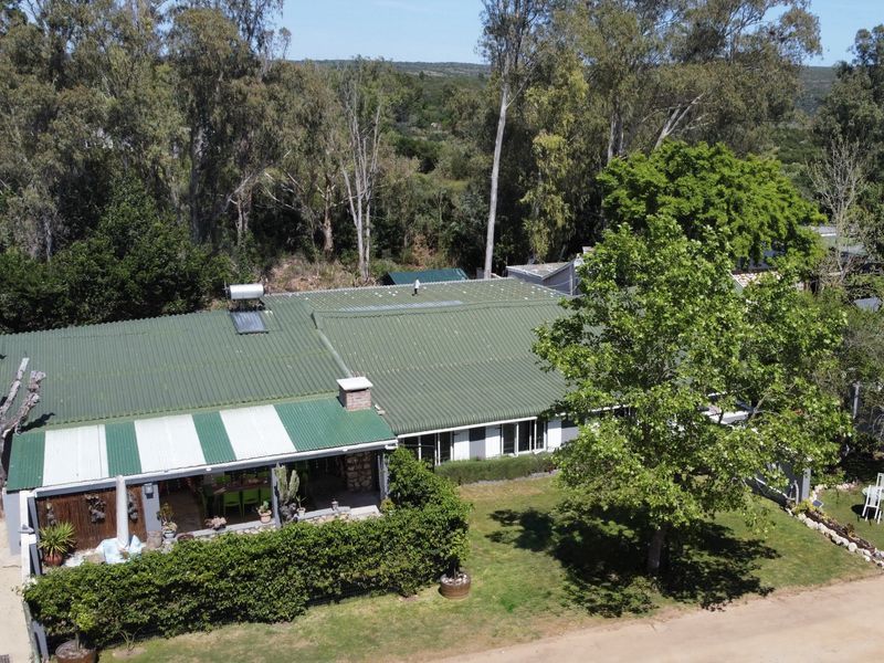 Aerial view of a residential property featuring a green corrugated metal roof, solar water heating system, and a spacious garden with a covered patio area.