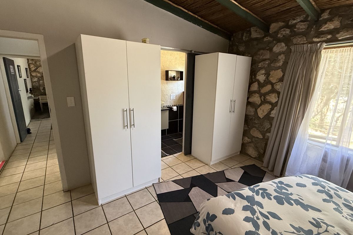 Bedroom featuring rustic exposed stone walls, timber beam ceiling, tiled flooring, and direct access to an en-suite bathroom.