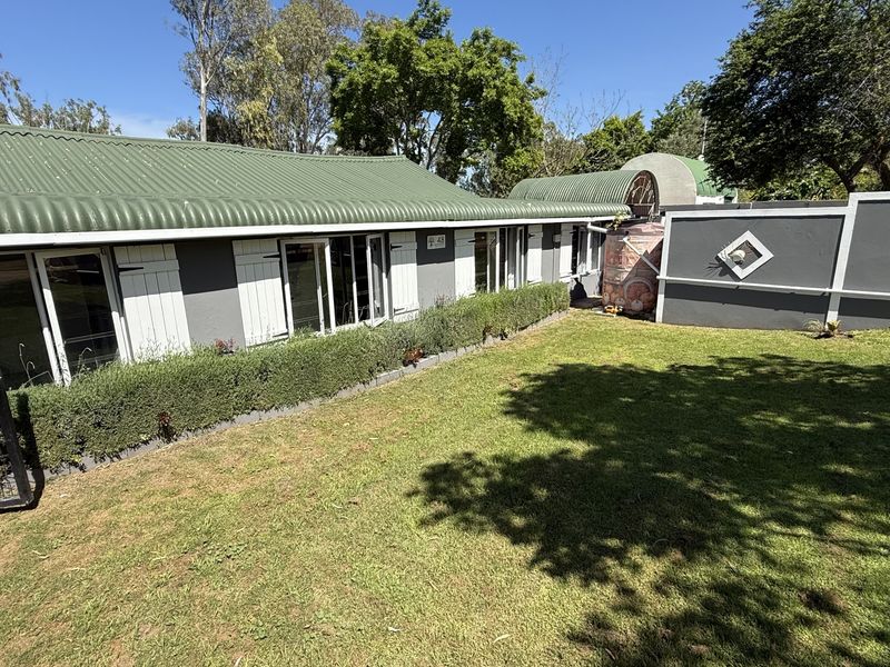 A well-maintained rear exterior view featuring a corrugated metal roof, a landscaped lawn, perimeter walling, and a water storage tank.