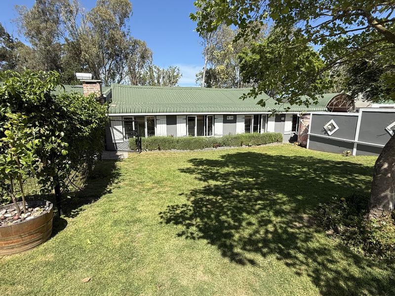 A well-maintained rear garden featuring a lush lawn, mature trees, and a clear view of the home's rear facade with a corrugated metal roof.